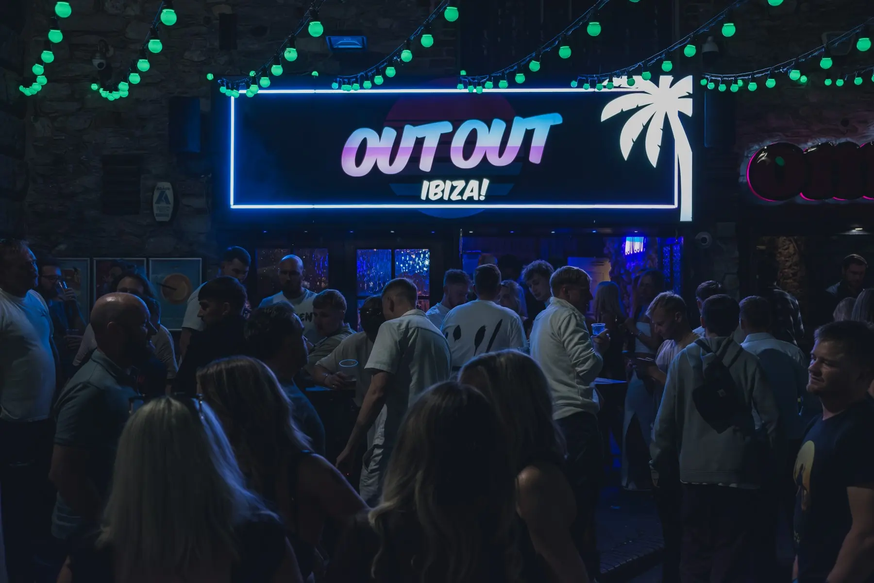 A crowded nightclub dancefloor with a large illuminated OutOut Ibiza sign above
