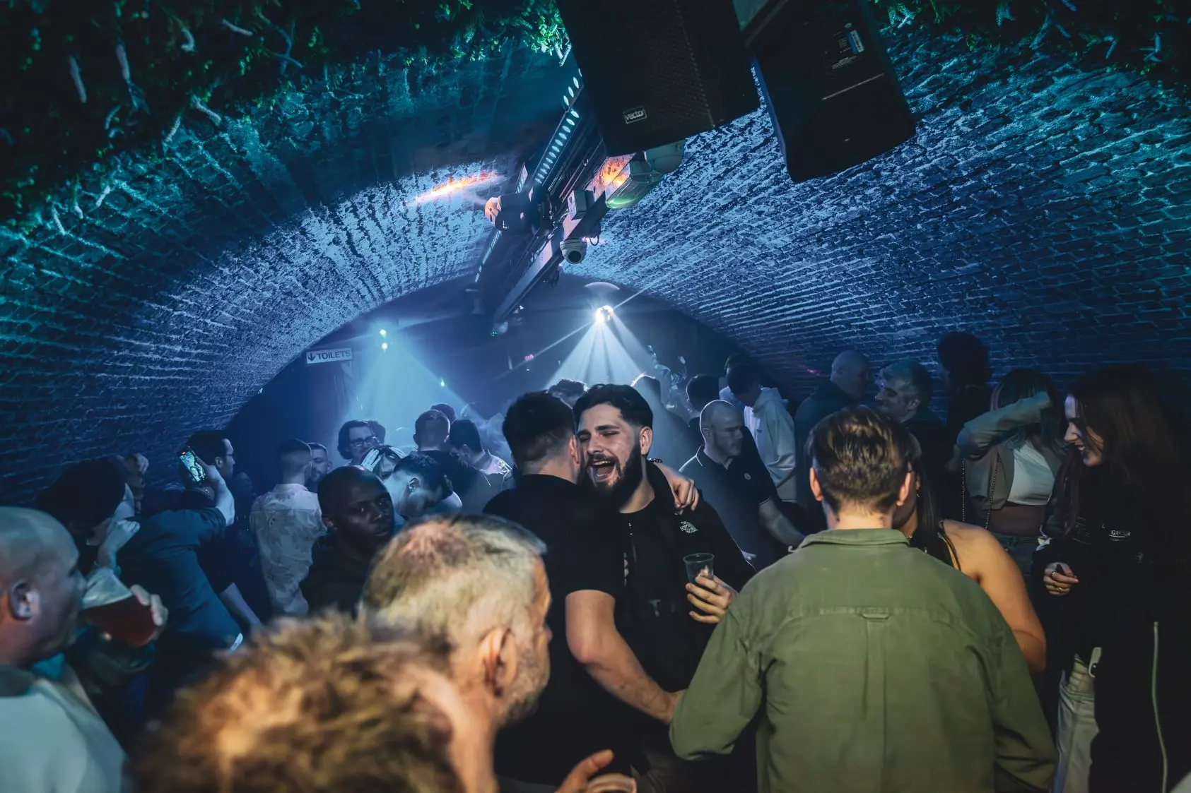 A crowded dancefloor in a nightclub with a curved ceiling with atmospheric lights