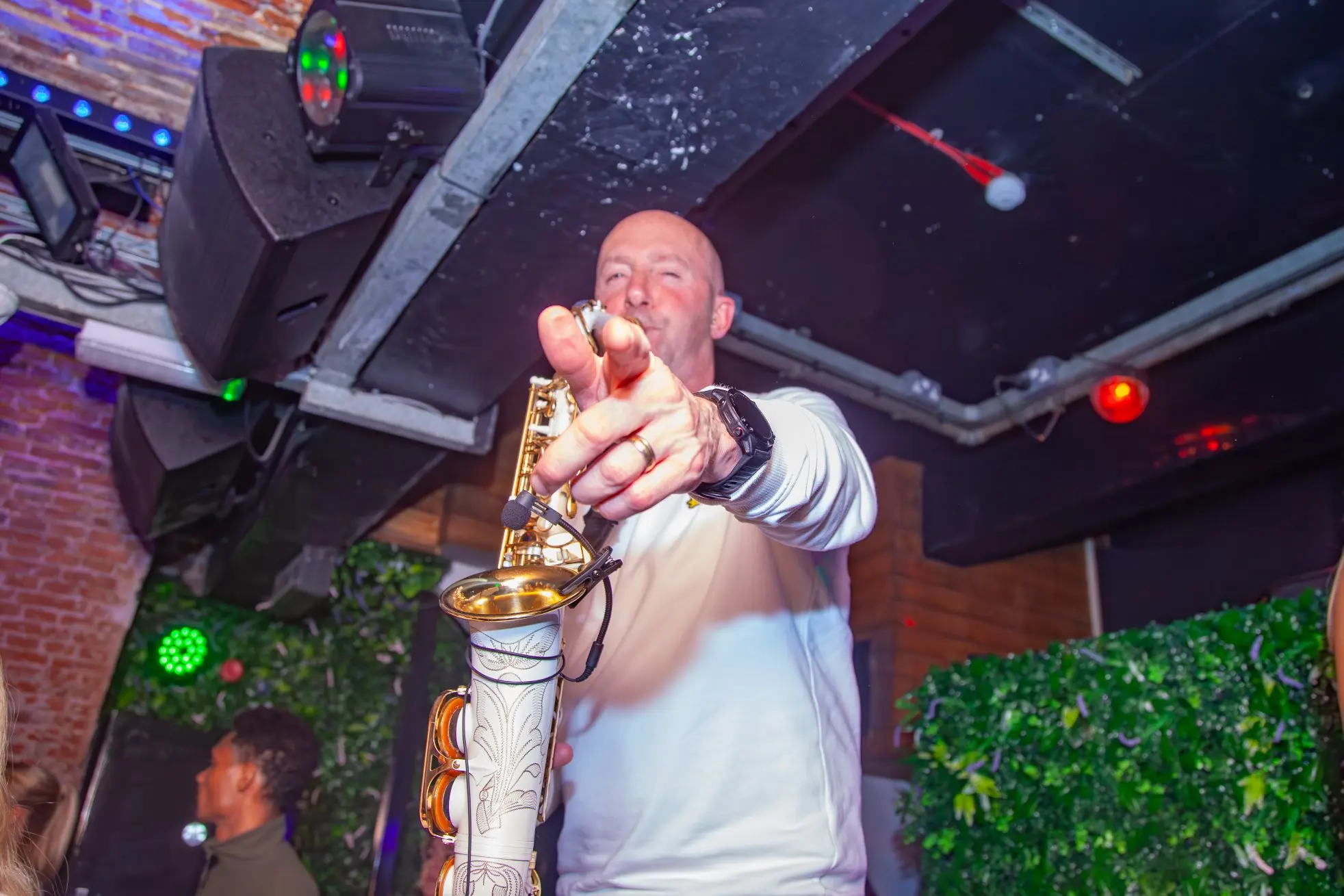 A saxophone player points into the camera whilst performing live music in the nightclub